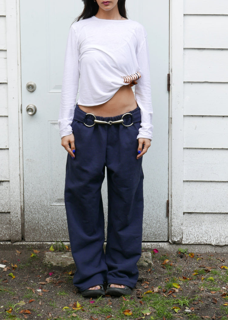 Person wearing a white shirt and blue sweatpants with bit standing in front of a white door.